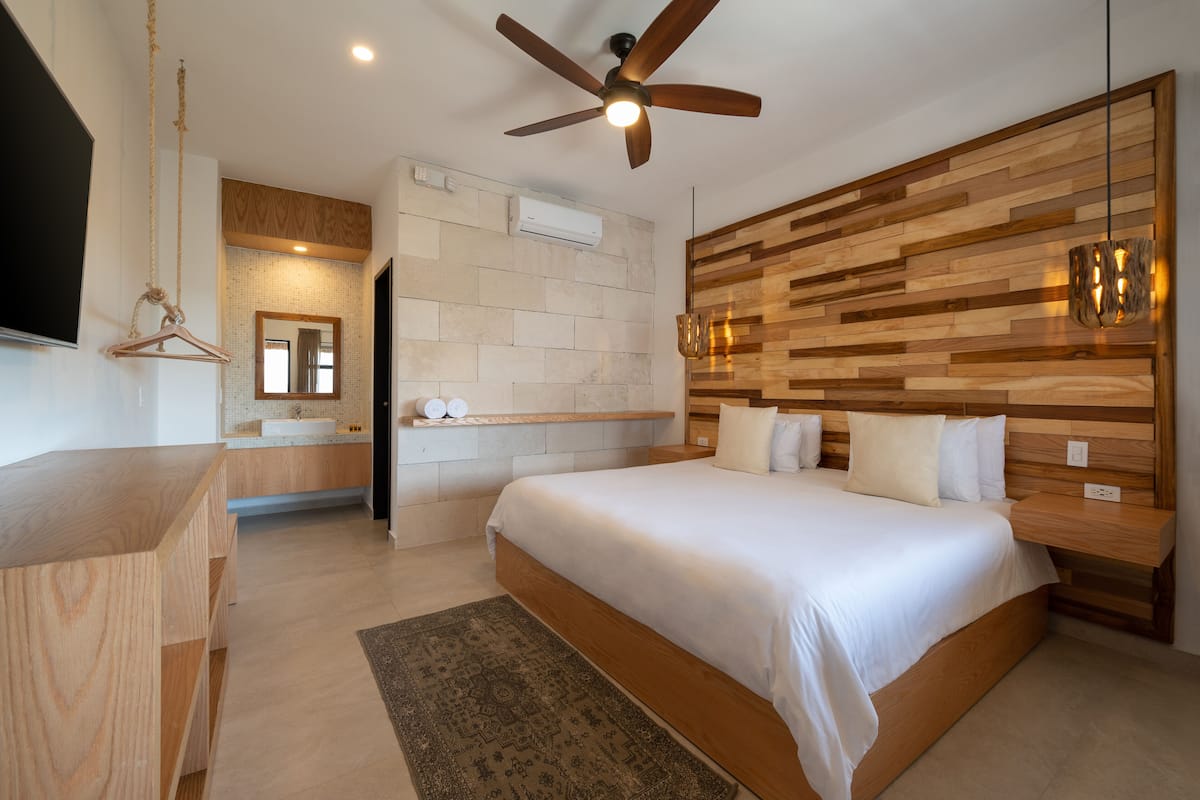 Un dormitorio moderno con cabecera de madera, ventilador de techo, mesita de noche y una cama grande.