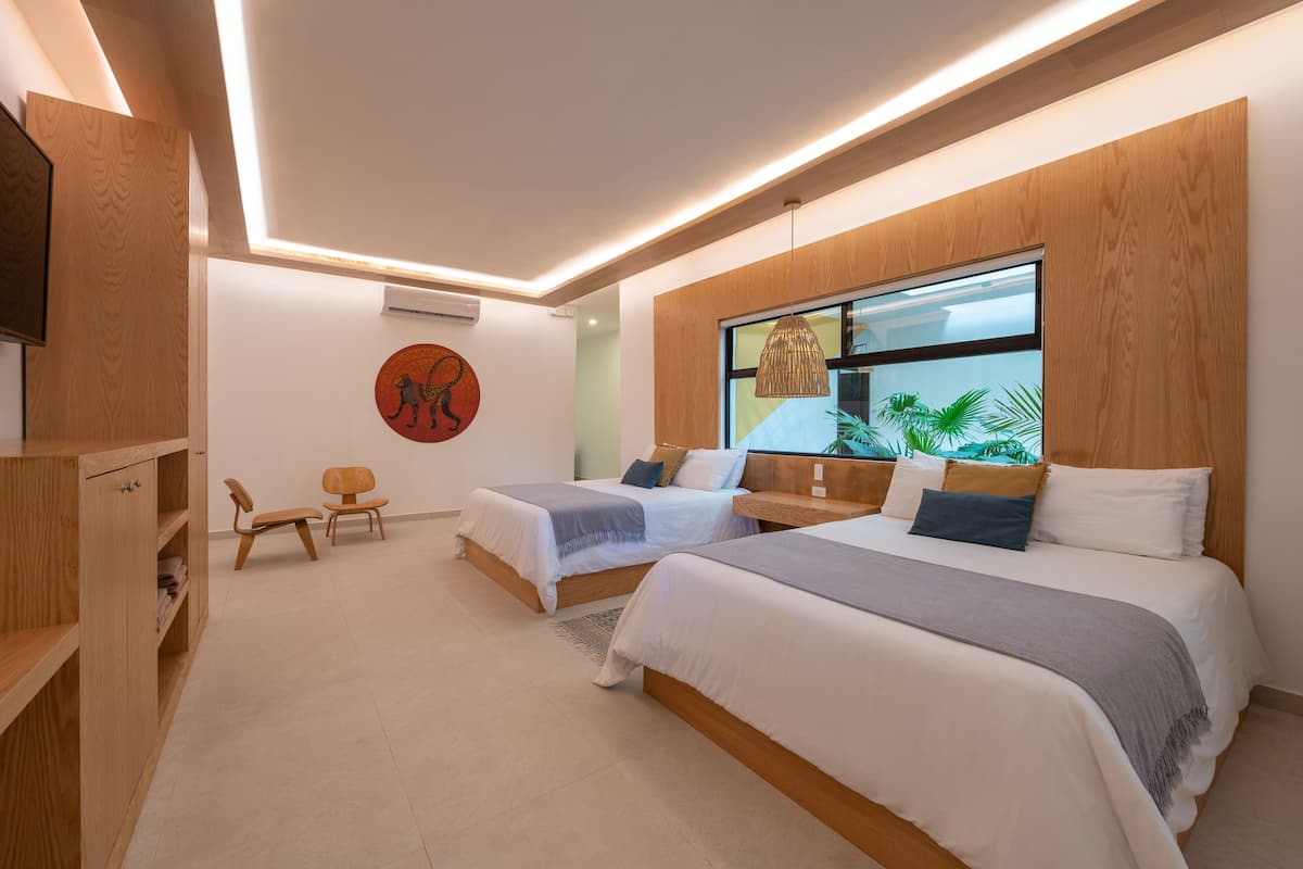 Un dormitorio moderno con dos camas, un armario de madera, un escritorio y un ventanal con vistas a zonas verdes.