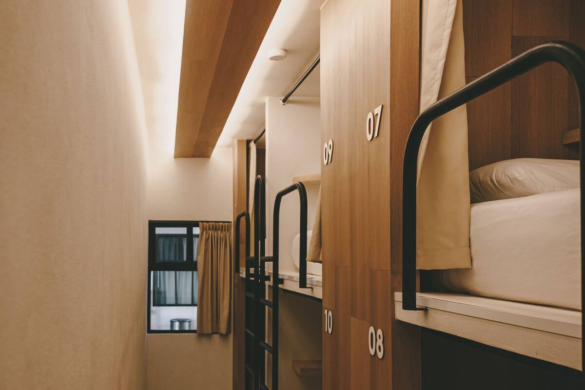 Un pasillo estrecho con literas numeradas del 07 al 10, paredes de madera y una ventana con cortinas.
