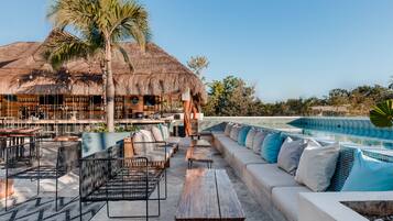 Un bar en la azotea con mesas al aire libre, piscina y una estructura cubierta de paja.