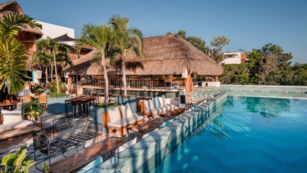 A resort pool area with a thatched-roof building, lounge seating, and a clear blue pool. - Mayan Monkey Tulum | Social Hotel (Tulum)