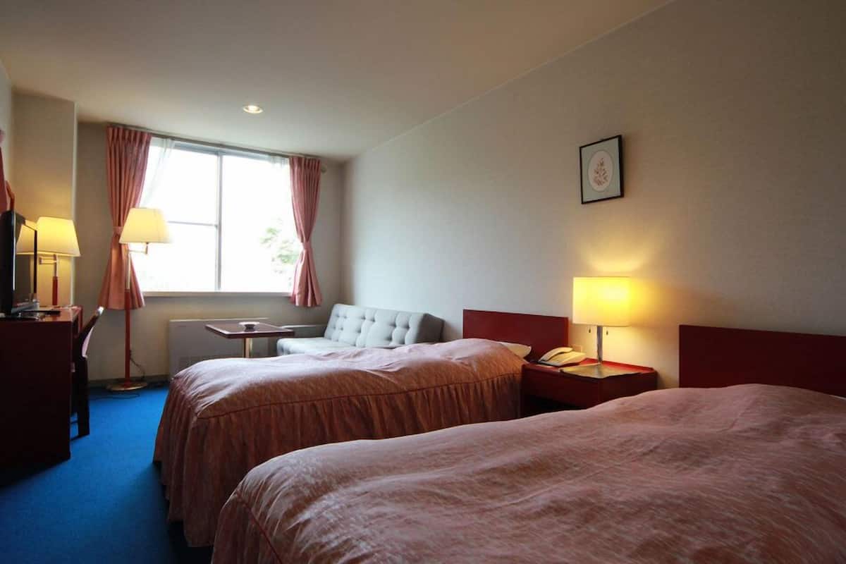 Ein Hotelzimmer mit zwei Betten, einem Schreibtisch, einem Stuhl, einem Tisch und einem fenster mit Vorhängen.