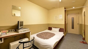 A hotel room with a bed, a desk with a computer, a chair, and a radiator. - Hotel Million (Muroran)