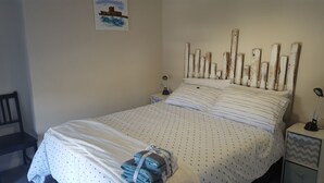 A neatly made bed with striped bedding, a headboard with vertical wooden slats, and a bedside table with a lamp. - The Tramway House (Carrickfergus)