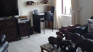 A living room with a glass coffee table, a leather sofa, a TV, a desk with a chair, and a window with curtains. - The Tramway House (Carrickfergus)
