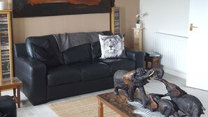 A living room with a black sofa, a coffee table with dinosaur figurines, a large abstract painting on the wall, and a bookshelf. - The Tramway House (Carrickfergus)