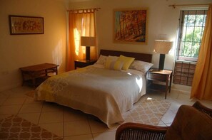 A bedroom with a large bed, two bedside tables, a chair, and a window with curtains. - The Gracious Villa (Gros Islet)