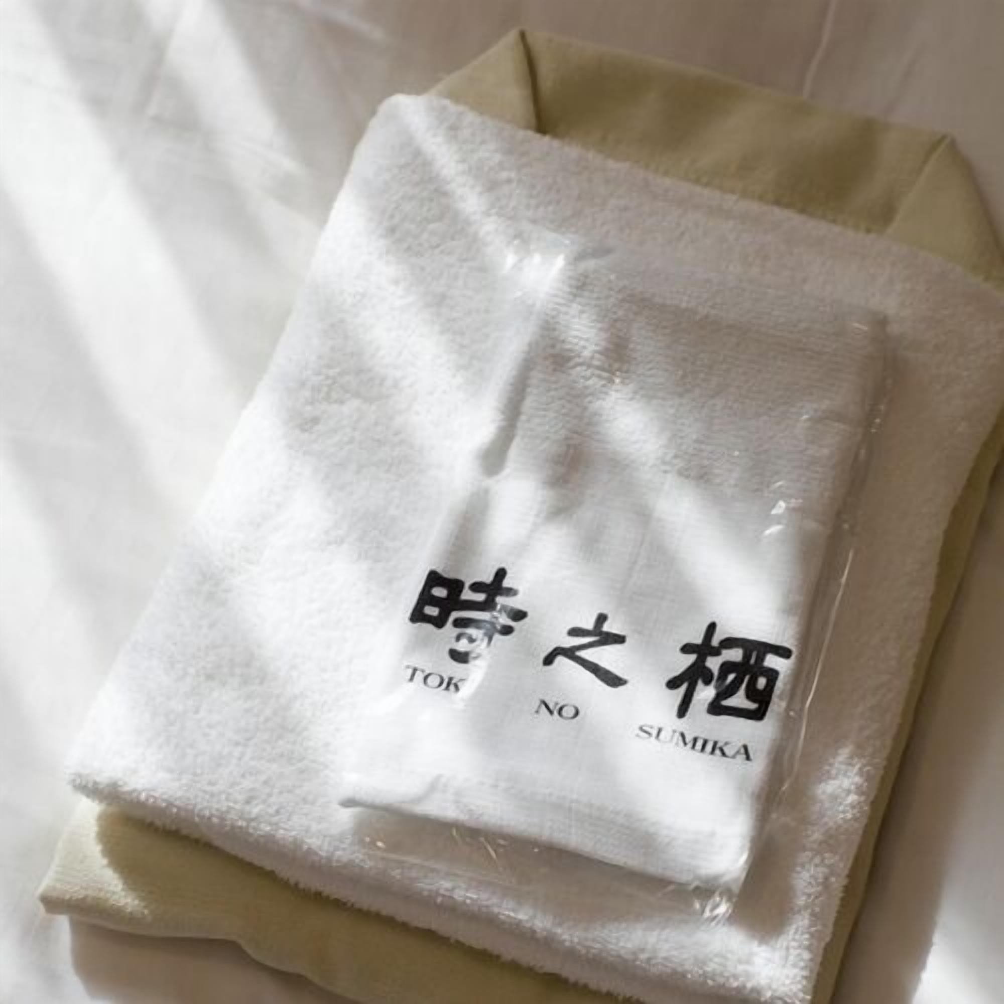 A white towel with Japanese characters and the word 'SUMIKA' on it, placed on a bed.