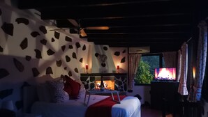 Ein gemütliches Schlafzimmer mit einem Bett, einem kleinen Tisch mit Kerzen, einem Kamin und einem Fernseher, der ein Lagerfeuer zeigt.