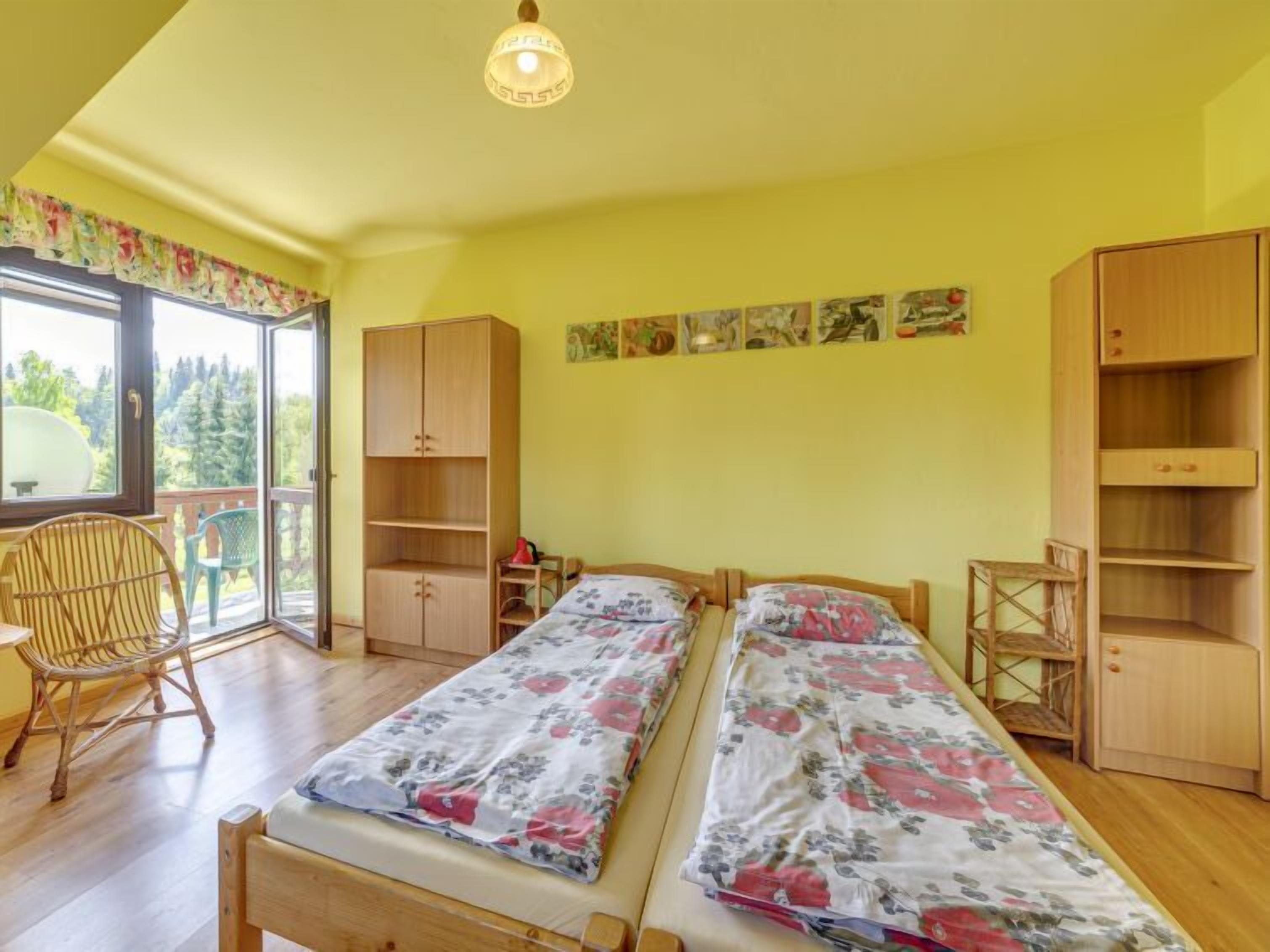 Une chambre avec deux lits, des meubles en bois et un balcon donnant sur la forêt.