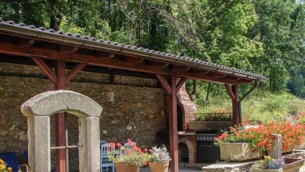 A stone building with a wooden pergola, outdoor grill, and potted plants. - Dom na Skraju by Interhome (Lubomierz/Gryfow Slaski)