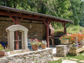 Um edifício de pedra com pérgola de madeira, churrasqueira e vasos de plantas.