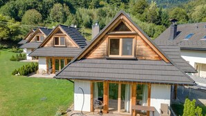 A wooden house with a sloped roof, large windows, and a deck with outdoor furniture. - Chaty Pod Beskidkiem by Interhome (Szczyrk)