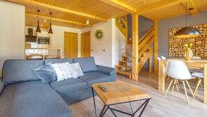 A modern living room with a grey sectional sofa, a wooden coffee table, and a staircase leading to a dining area with a wooden table and chairs. - Chaty Pod Beskidkiem by Interhome (Szczyrk)