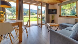 A spacious living room with a wooden ceiling, a sofa, a TV mounted on the wall, and a large window offering a view of the outdoors. - Chaty Pod Beskidkiem by Interhome (Szczyrk)