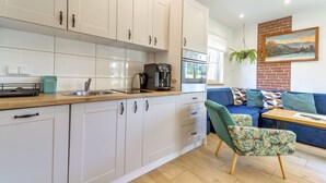 A modern kitchen with white cabinets, a coffee machine, and a sink. There is a blue sofa with patterned cushions and a green chair. A painting hangs on the wall above the sofa. - Siglanów by Interhome (Wisla)