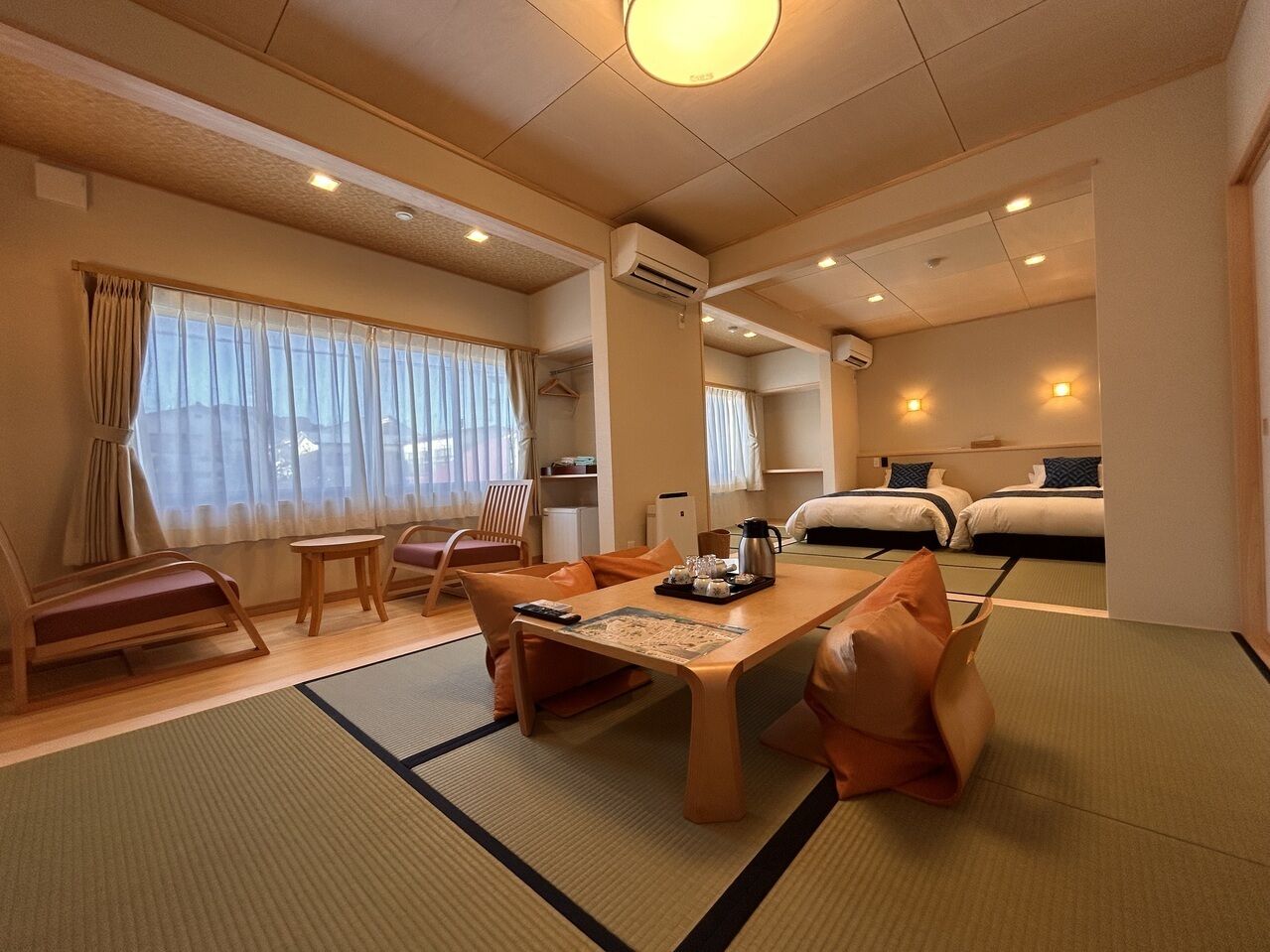 Um quarto tradicional japonês com tatame, uma mesa baixa com almofadas, um sofá, uma cama e uma pequena mesa com chá.