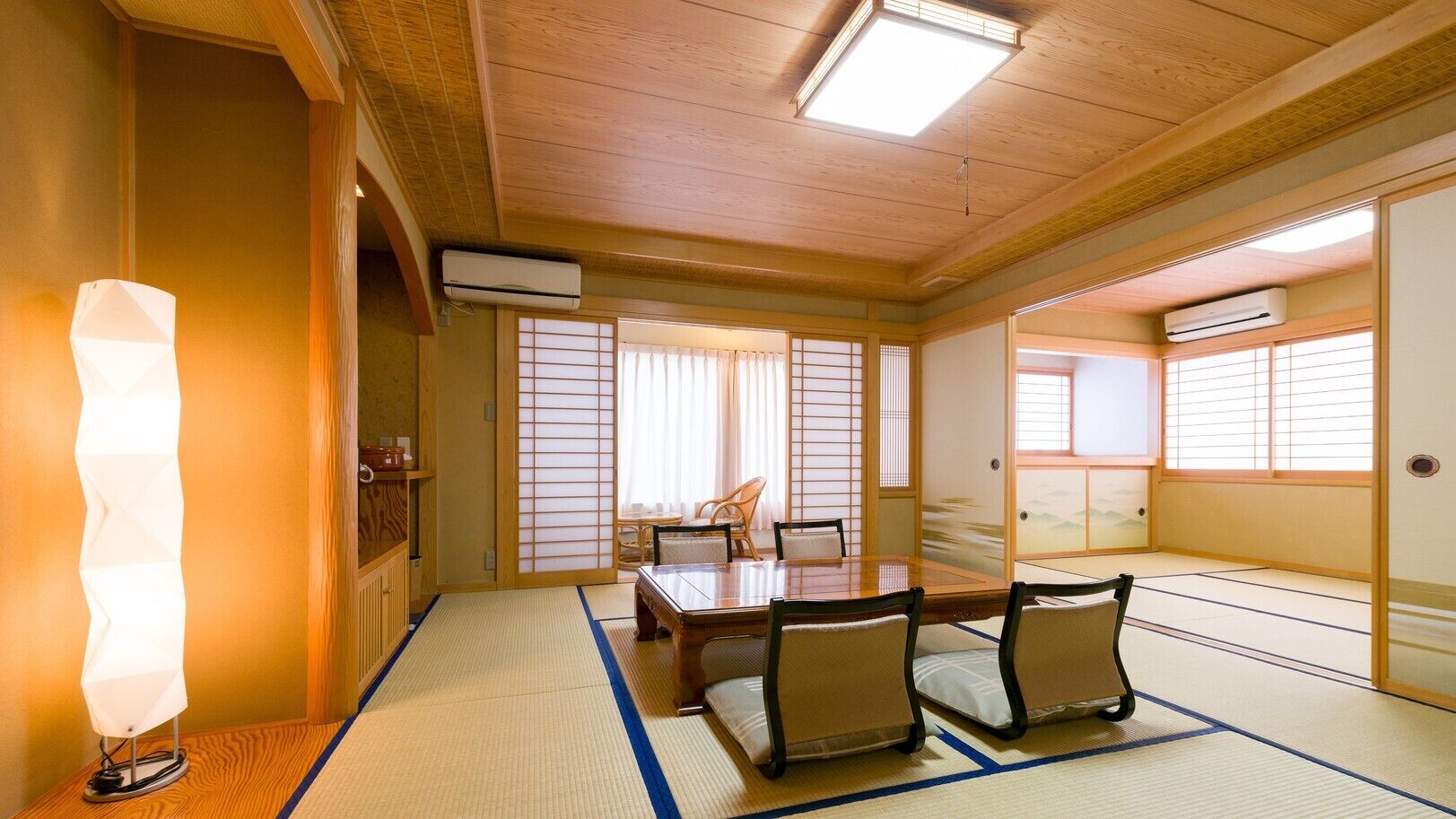 Um quarto japonês tradicional com tatames, uma mesa baixa com cadeiras, portas deslizantes e um ventilador de teto.