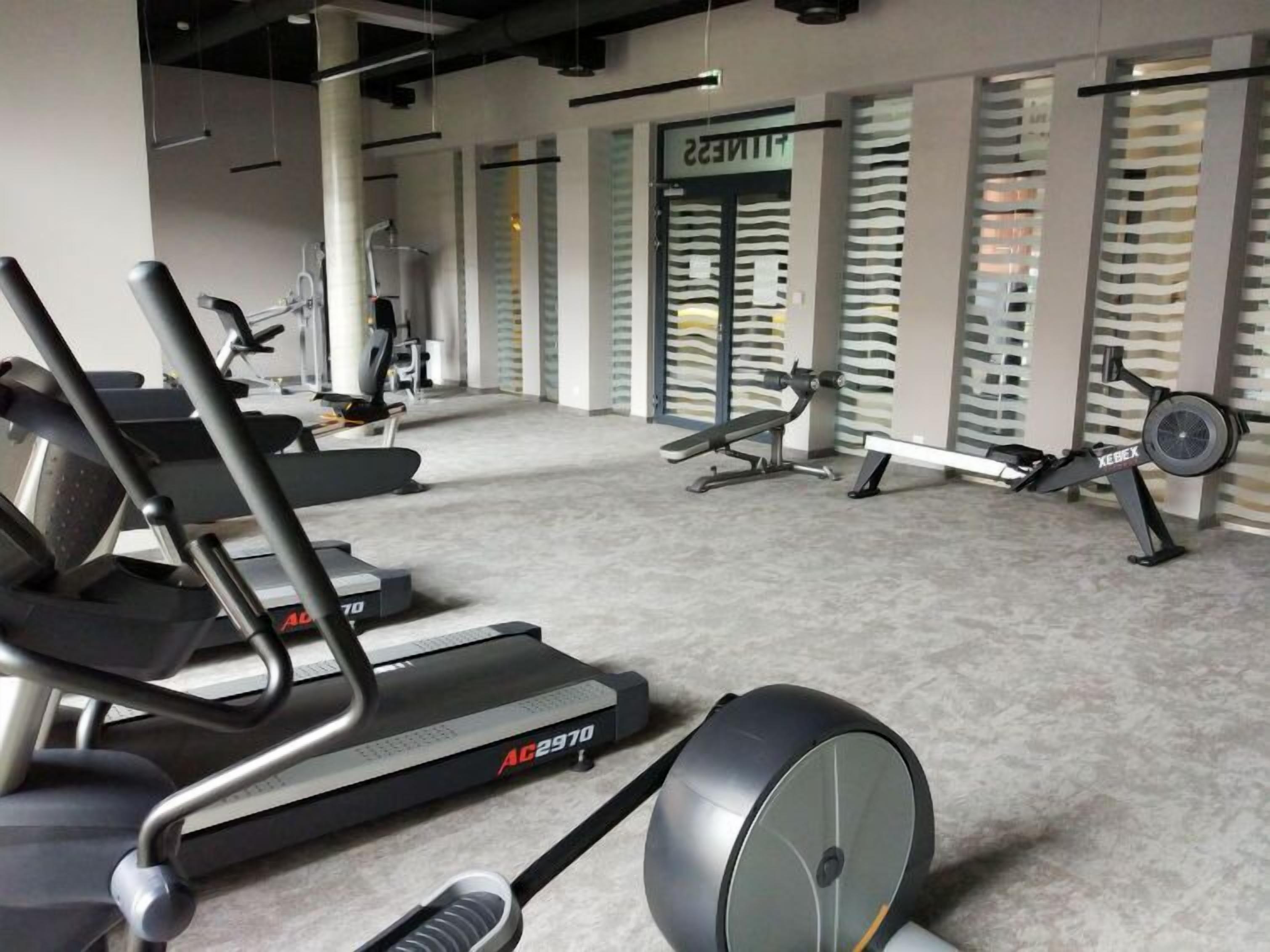 Ein modernes Fitnessstudio mit Cardiogeräten, Krafttrainingsgeräten und einer Spiegelwand.