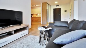 Un salon moderne avec un téléviseur à écran plat, un canapé gris et une petite table d’appoint.