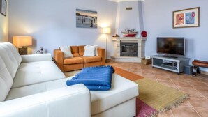 A living room with a white sofa, a brown sofa, a fireplace, a television, and artwork on the walls. - Grand Beach Hit by Interhome (Pêra)