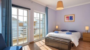 A modern hotel room with a large sliding glass door leading to a balcony, a bed with a wooden headboard, a bedside table with a lamp, and a framed picture on the wall. - Grand Beach Hit by Interhome (Pêra)