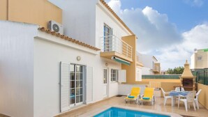 A modern outdoor pool area with a clear blue pool, white walls, and a balcony with yellow chairs. - Grand Beach Hit by Interhome (Pêra)