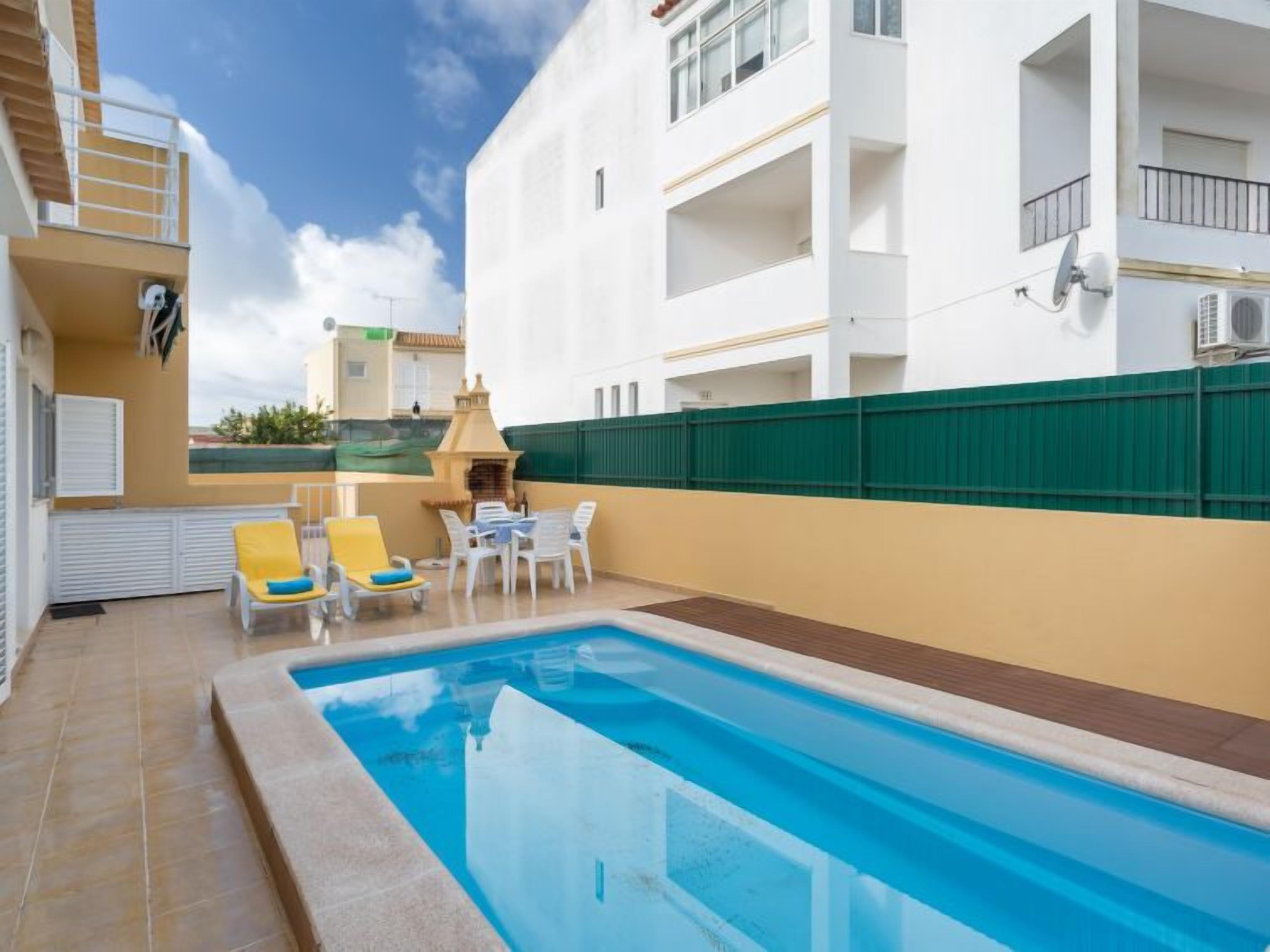 Ein Swimmingpool mit Liegestühlen und einem Tisch, umgeben von einem weißen Gebäude mit Balkonen.