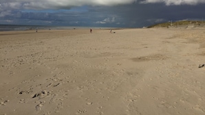 Een breed zandstrand met voetsporen en enkele mensen verspreid over het strand.