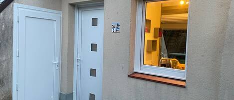 A building entrance with a white door and a window with a yellow interior.