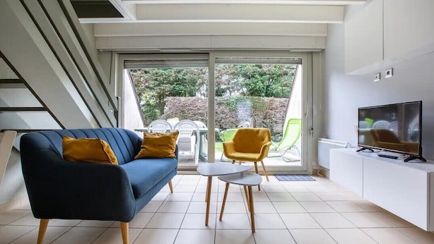 Een moderne woonkamer met een bank, twee stoelen, een televisie en een schuifdeur naar een tuin.