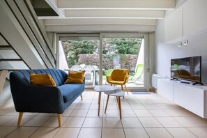 A modern living room with a sofa, two chairs, a TV, and a sliding glass door leading to a garden. - Cottage "Opale", 900m beach with terrace and Wifi - Stella beach (Le Touquet) (Cucq)
