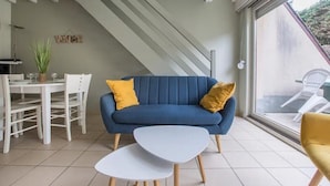 Een moderne woonkamer met een blauwe bank, twee witte bijzettafels en gele kussens.