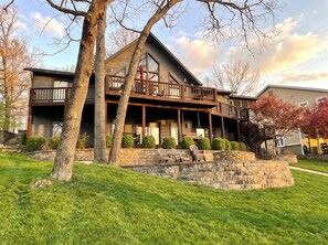 A two-story building with a balcony, stone retaining wall, and green lawn. - Peaceful Lakefront Retreat with Private Dock, Fire Pit, Kayaks (Gravois Mills)