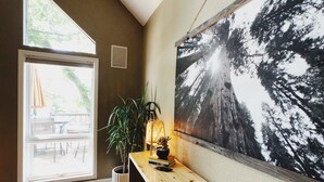 Une pièce avec une grande fenêtre, un banc en bois, une plante en pot et un tableau accroché au mur.