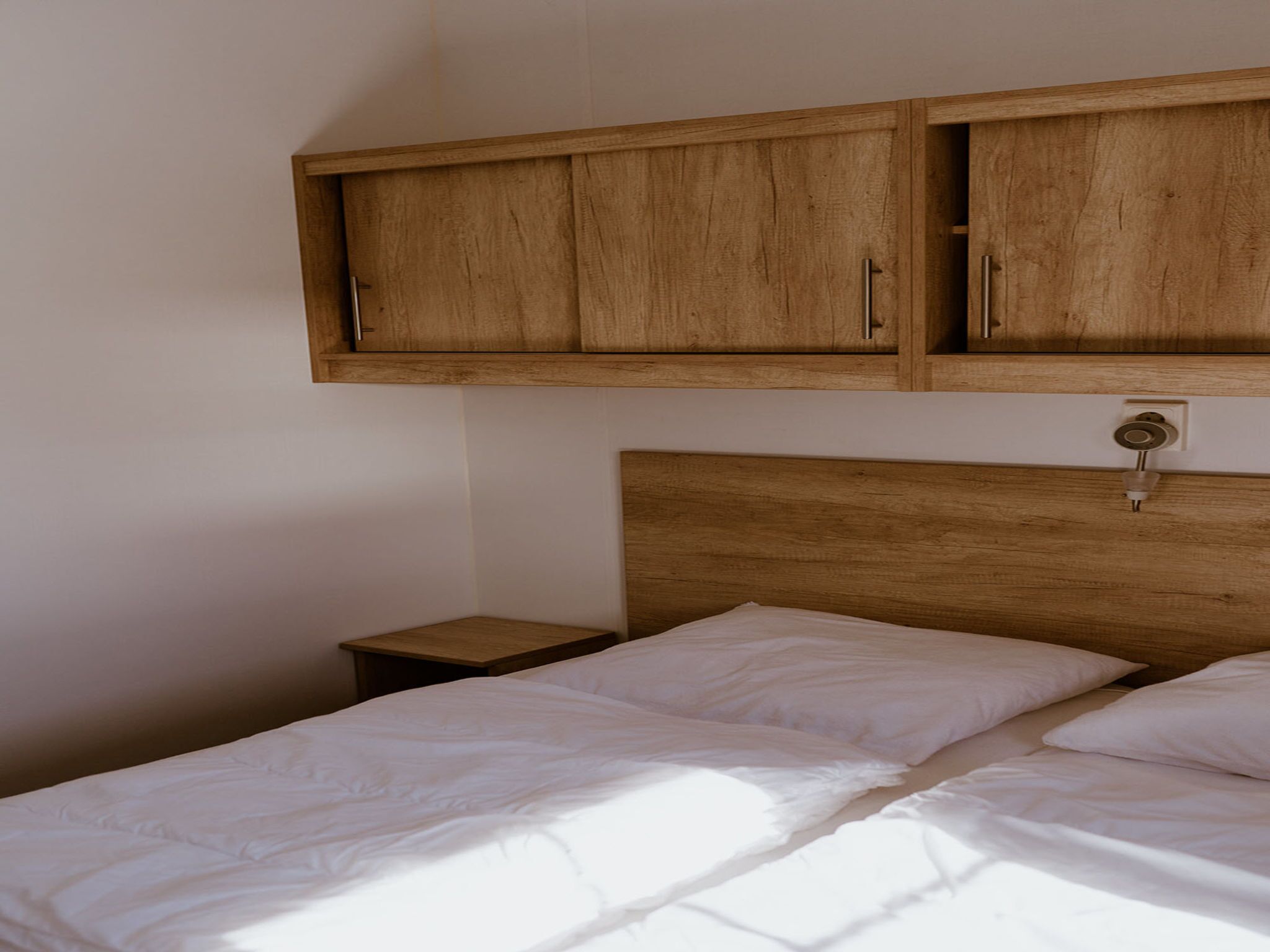 A bedroom with a wooden headboard, two single beds with white linens, and a wooden cabinet above the beds.
