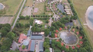 Vue aérienne d’un quartier résidentiel avec de nombreuses maisons, un grand étang circulaire et un terrain de sport.