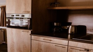 Una cocina compacta con armarios de madera, horno integrado, cafetera y hervidor.
