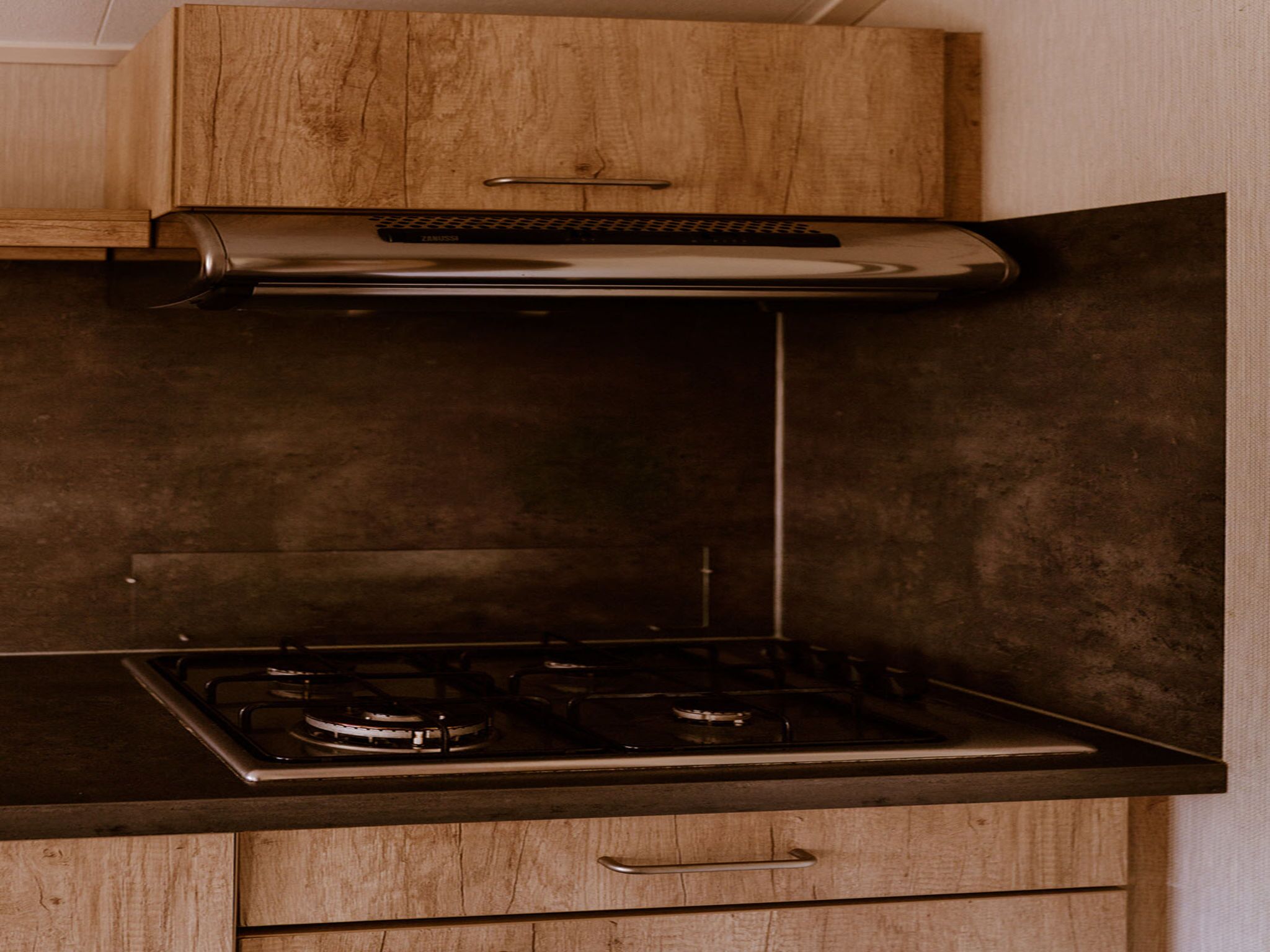 A kitchen with a stainless steel range hood, a gas stove, and wooden cabinets.