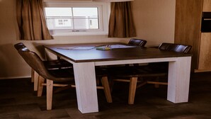 Un comedor con mesa y sillas de madera, lámpara colgante y ventana con cortinas.