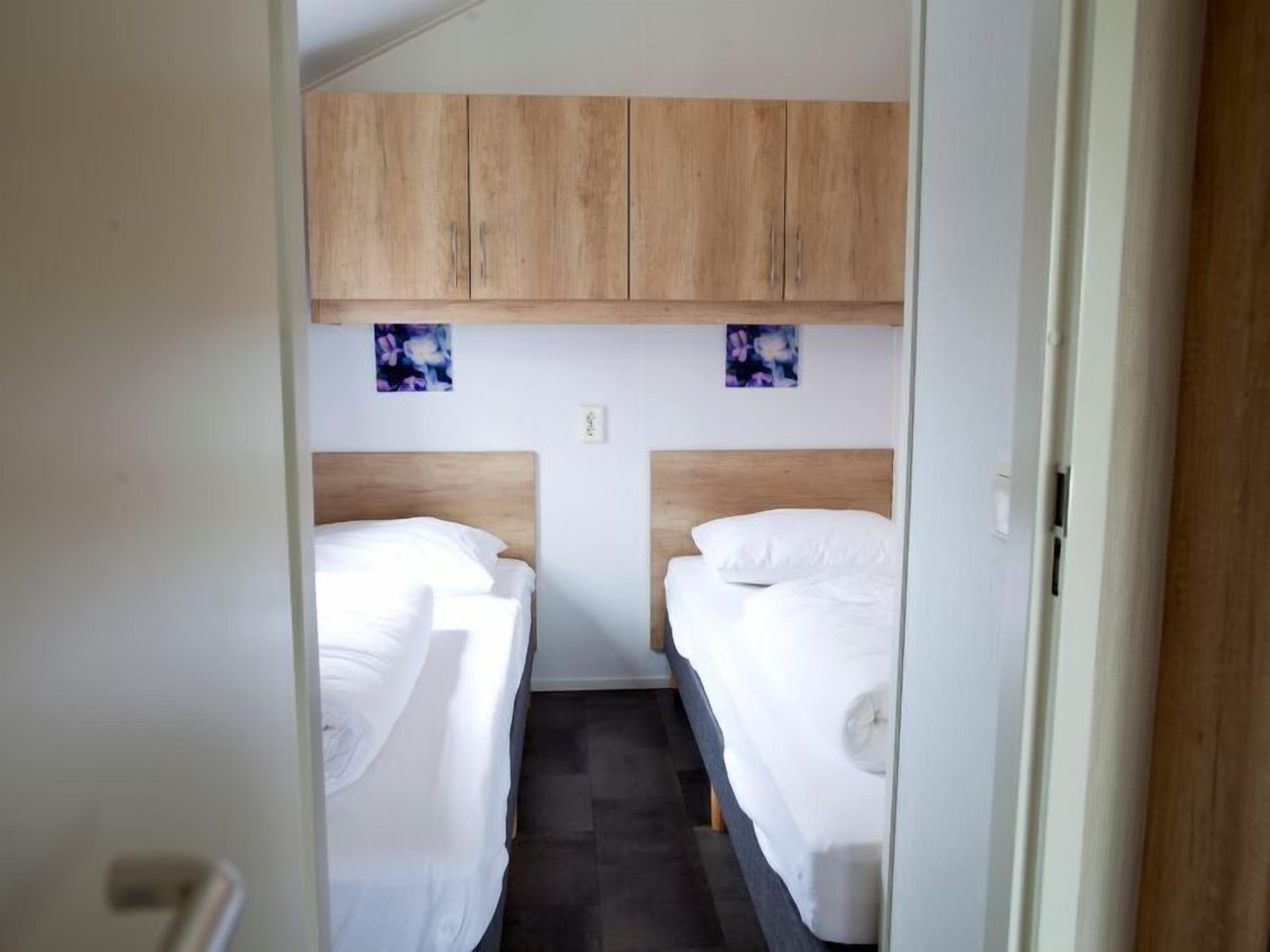 A small, compact room with two single beds, wooden headboards, and a small shelf above the beds.