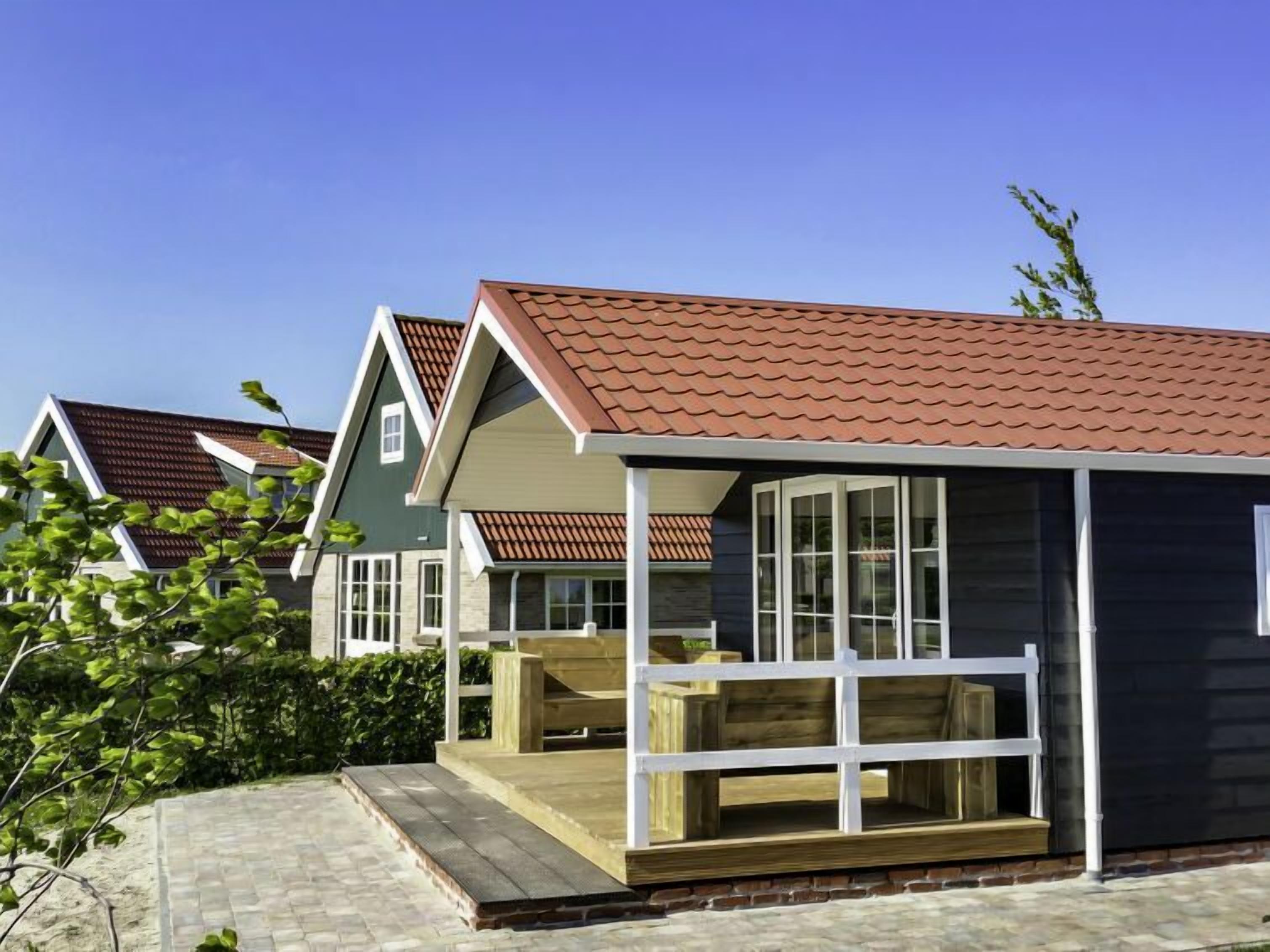 Een modern huis met een overdekte veranda, een klein terras en een met baksteen bestraat pad dat naar de ingang leidt.