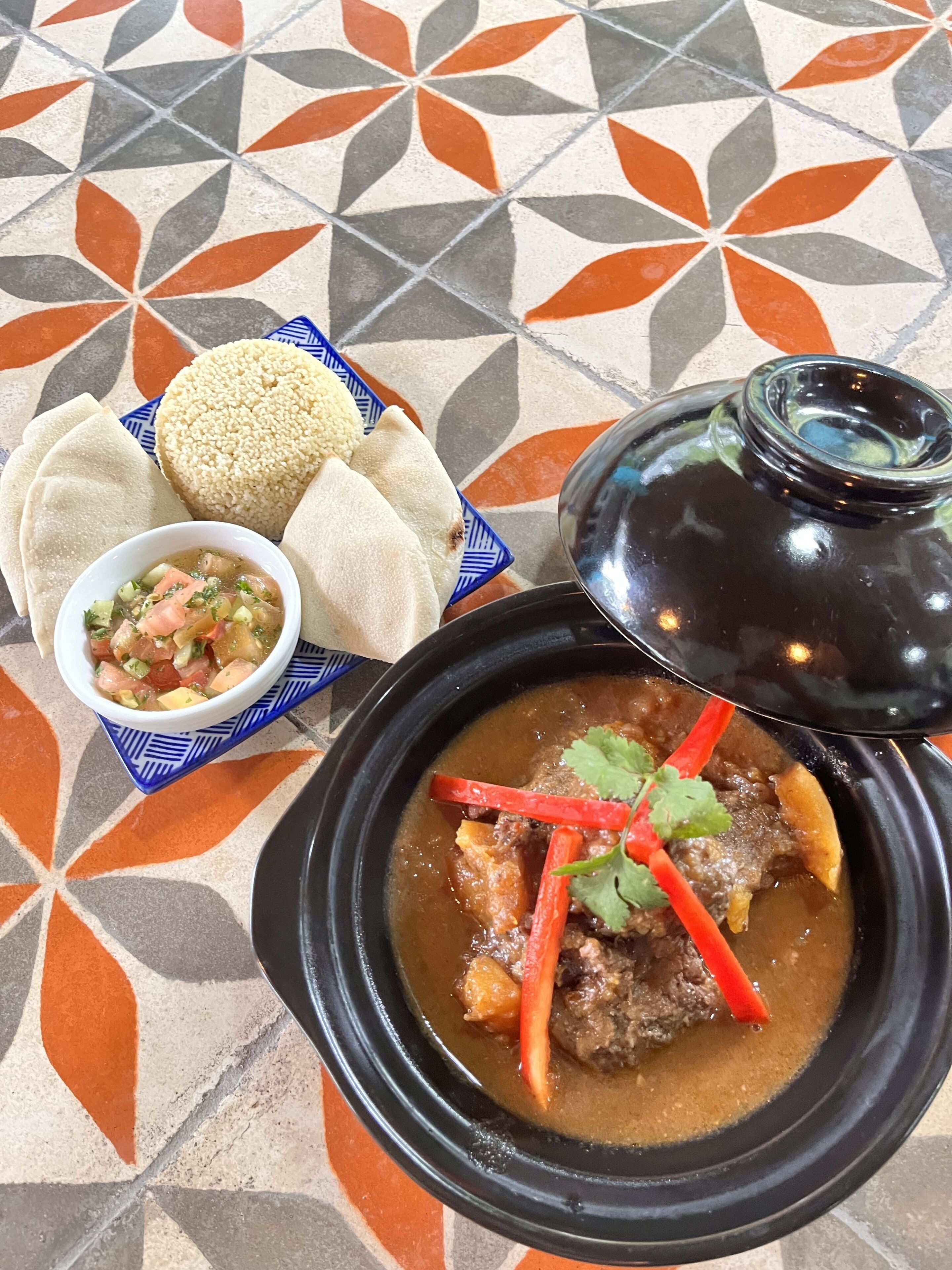 A meal with a black pot, a bowl of salad, and flatbread on a patterned table.