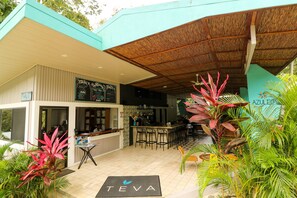 A modern outdoor cafe with a bar area, seating, and tropical plants. - Téva Eco Retreat - Hostel (Quepos)