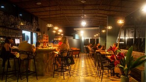 A restaurant with a bar area, multiple tables and chairs, and a patterned floor. - Téva Eco Retreat - Hostel (Quepos)