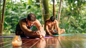 Two people practicing yoga on a wooden floor with a candle in the foreground. - Téva Eco Retreat - Hostel (Quepos)