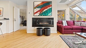 Uma sala de estar moderna com lareira, um sofá vermelho e uma janela ampla com vista para a folhagem outonal.