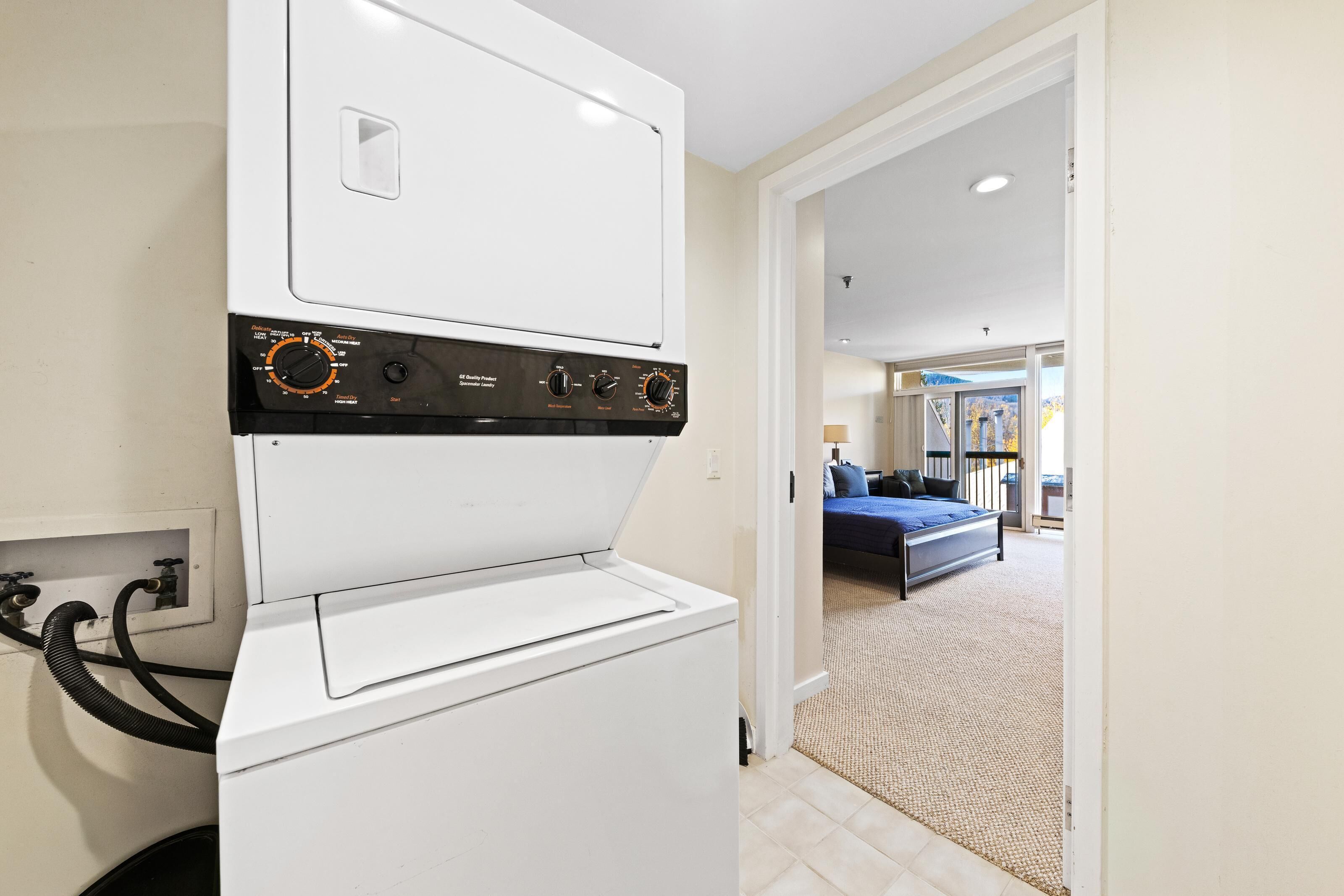 A front-loading washer and dryer unit with control knobs, a power cord, and a visible electrical outlet.