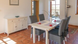 A dining area with a white table, four chairs, a vase with branches, and a framed picture on the wall.