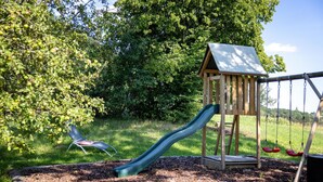 A playground with a slide, swings, and a wooden playhouse.